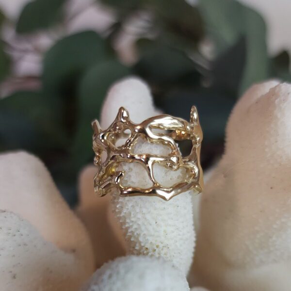 Gold wide-band coral-textured ring resting on white coral prop