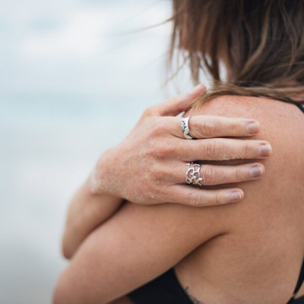 Two silver rings worn on hand resting on shoulder at beach