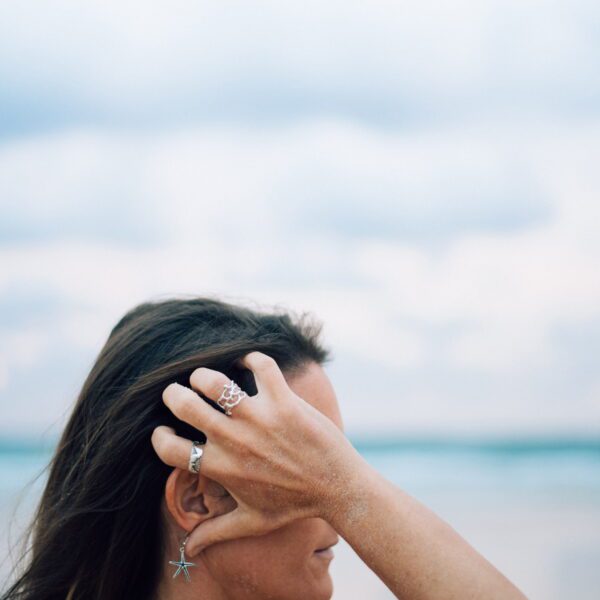 Silver coral-branch ring worn on finger at beach, with starfish earring visible