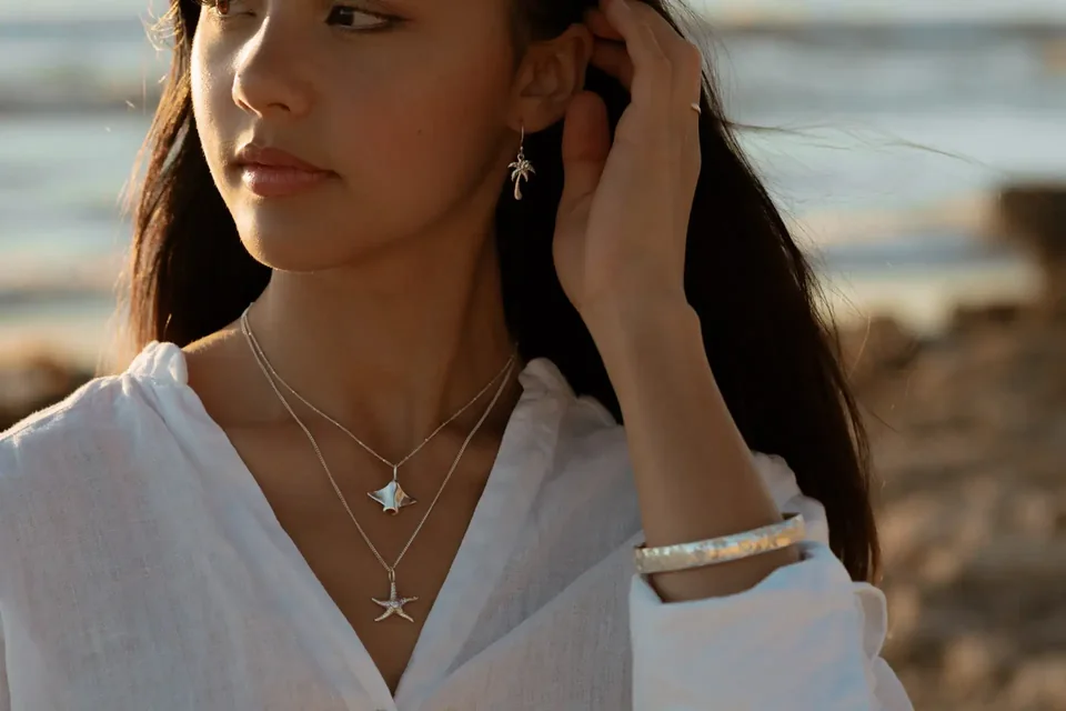 Woman in a white linen shirt wearing layered Kaikoa pendants