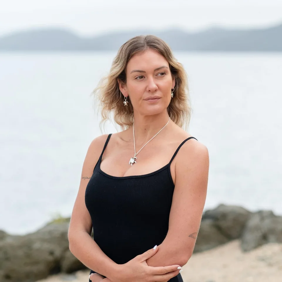 Woman by the sea wearing a sterling silver turtle pendant and earrings