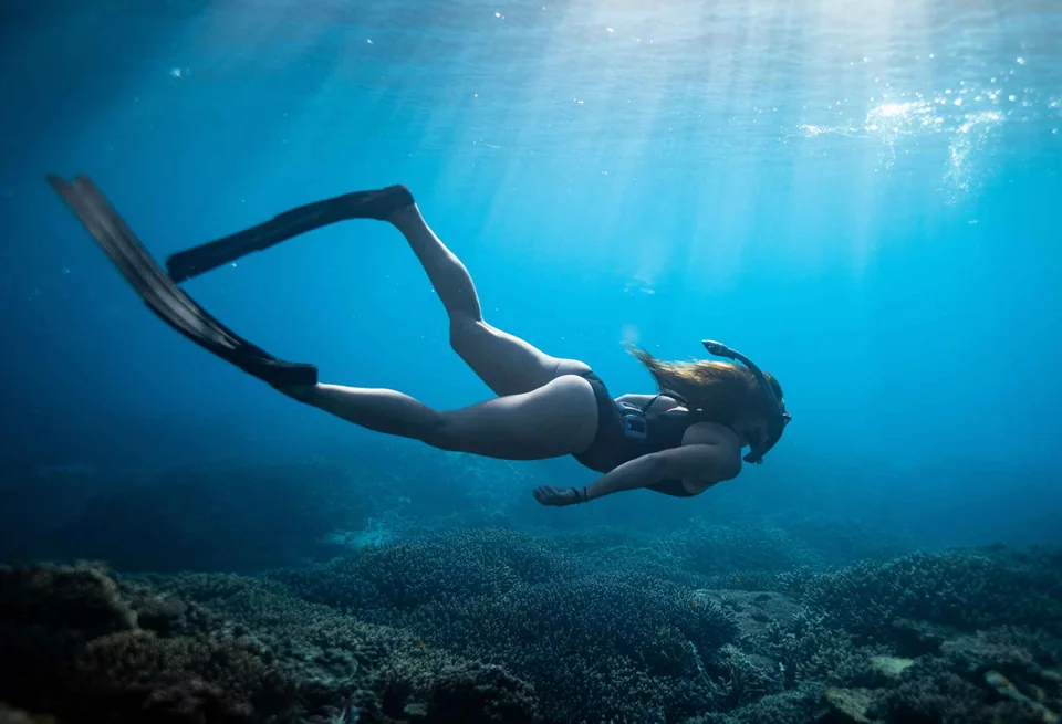 Freediver gliding underwater through shafts of sunlight