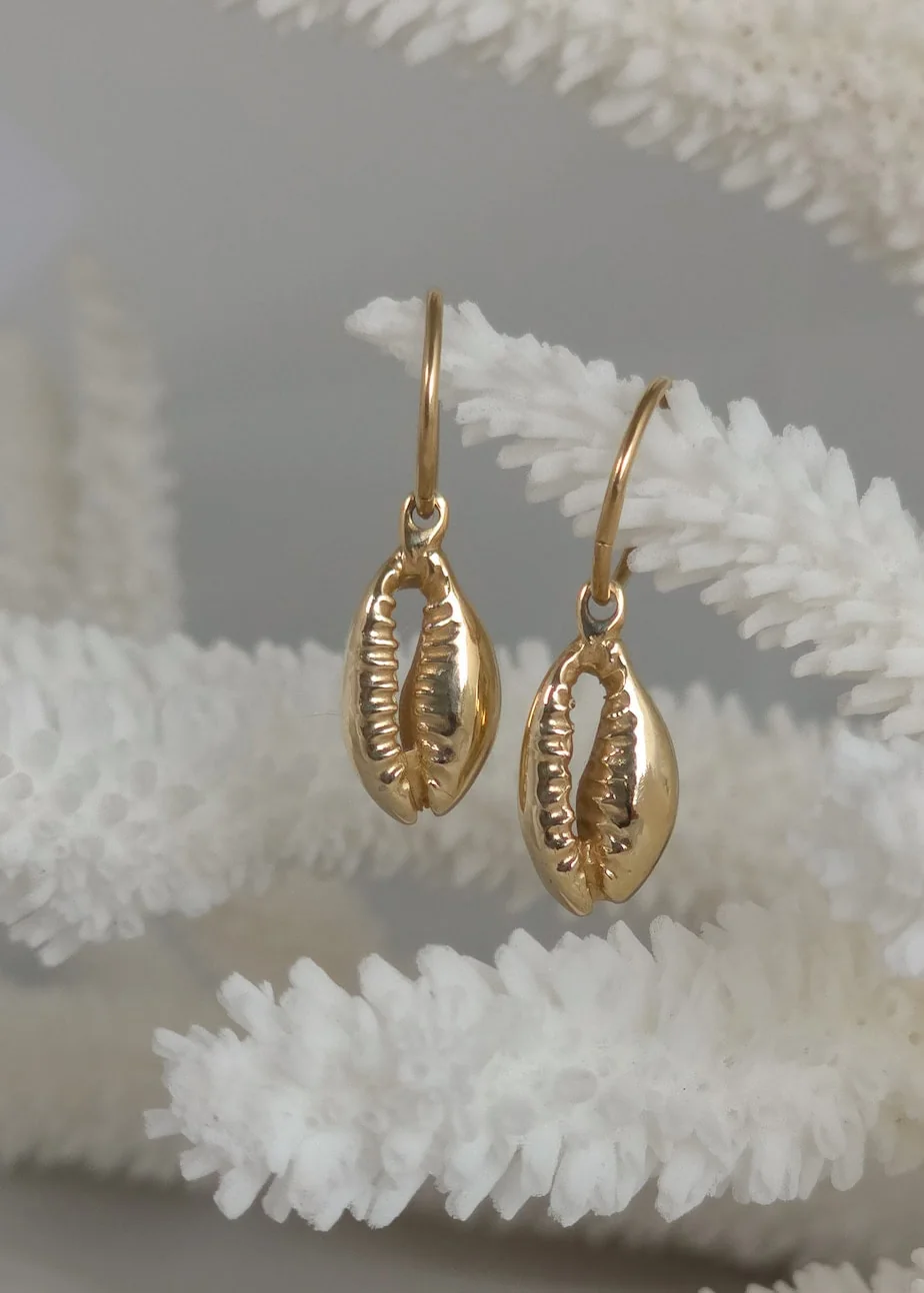 Solid gold cowrie shell earrings hanging on white coral